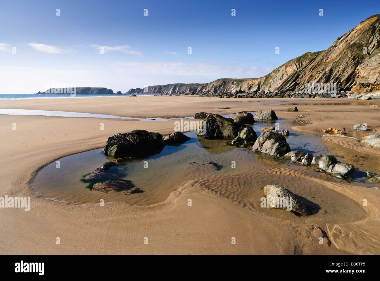 Deserted pristine beach at Marloes in Pembrokeshire at low tide with a clear rock-pool in the foreground on a sunny day. Stock Photo