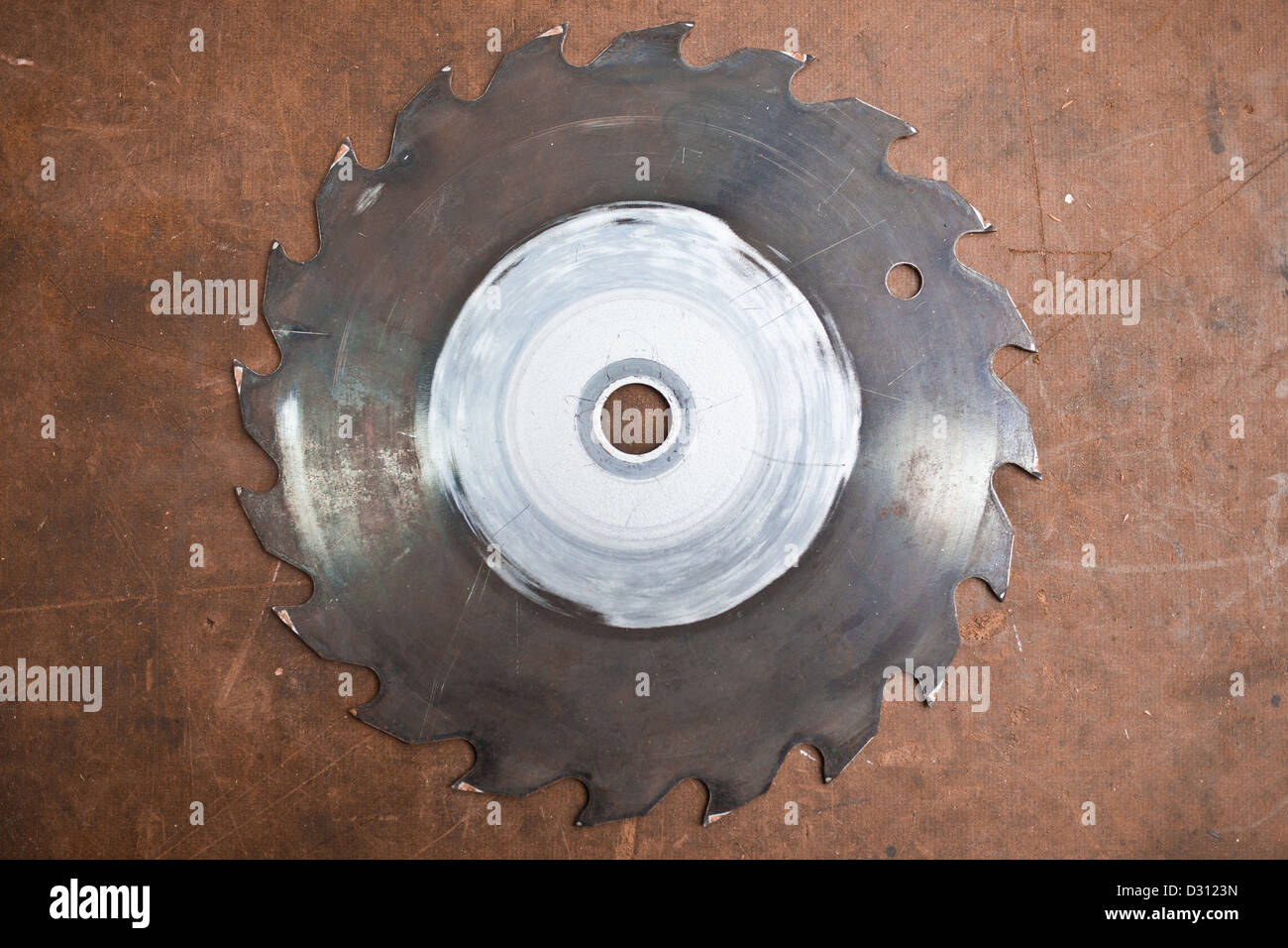 A metal, rusty, circular saw blade on a brown table top. Stock Photo