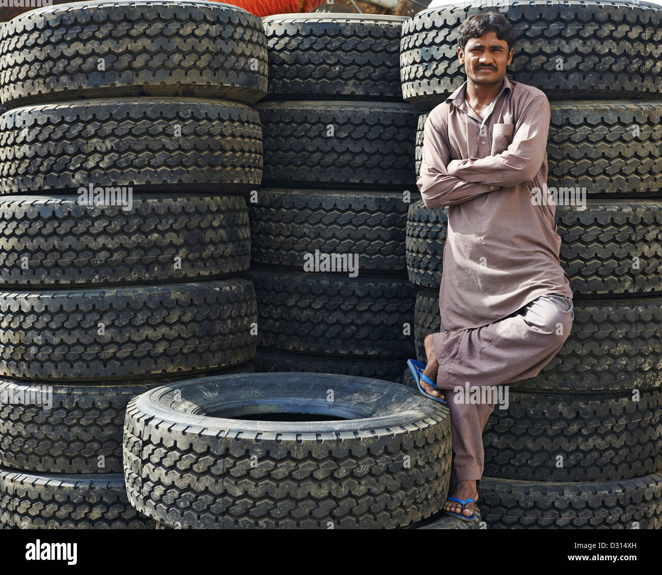 A man crosses his arm and raises his leg in front of a huge stack of tires Stock Photo