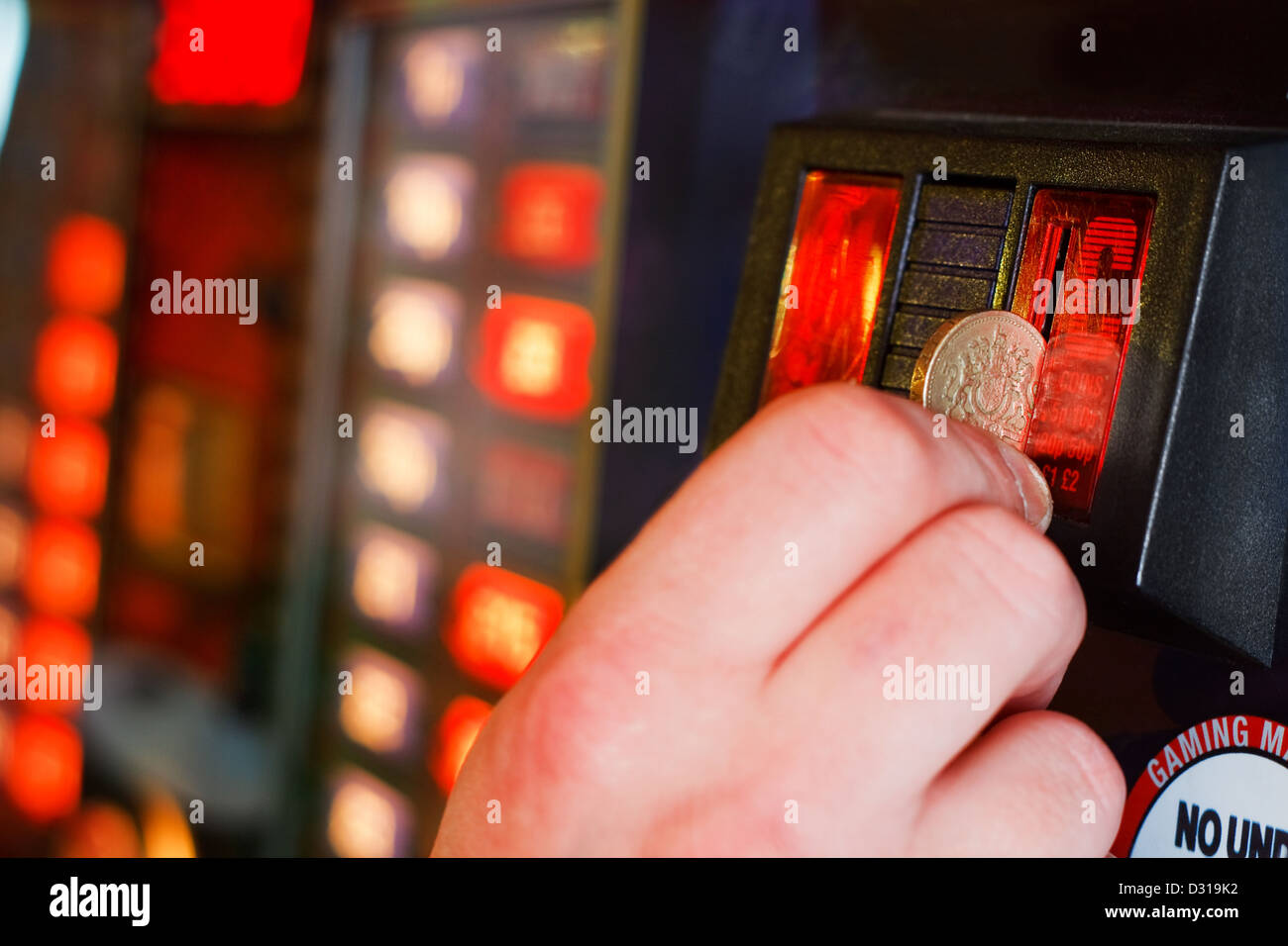 Gambler Inserts pound coin into gambling machine at casino Stock Photo