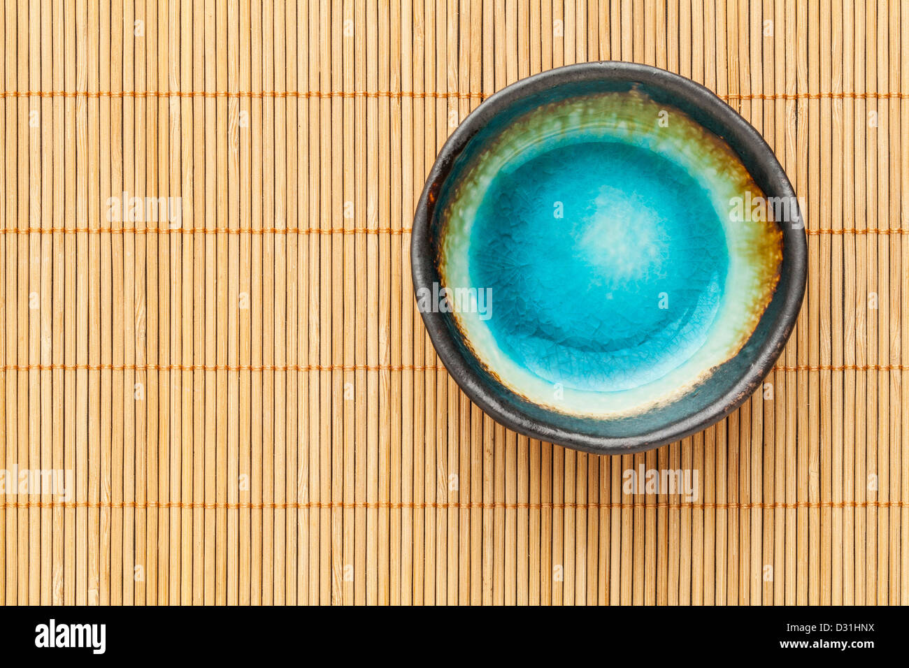 small empty ceramic bowl (sauce dish) with blue enamel on bamboo place mat Stock Photo