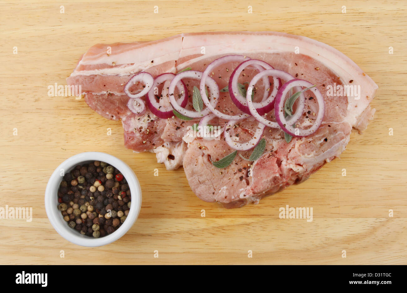 Pork chop dressed with red onion sage and pepper with mixed peppercorns in a ramekin on a wooden board Stock Photo