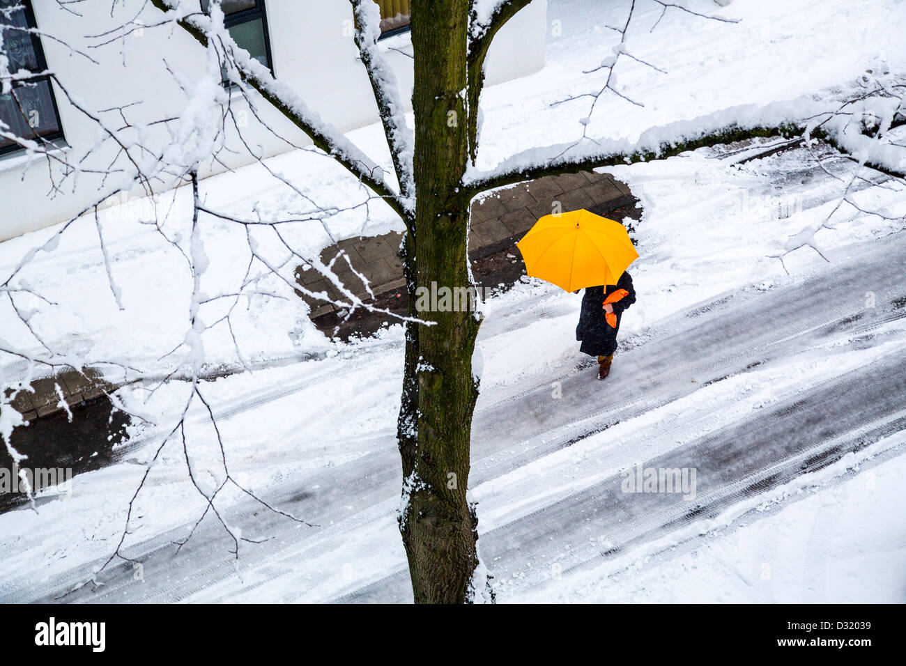 Person with a yellow umbrella walks on a snow covered street. Stock Photo