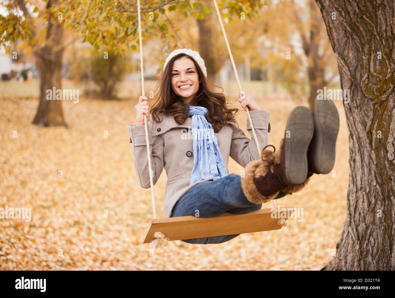 Caucasian woman sitting on swing in autumn leaves Stock Photo