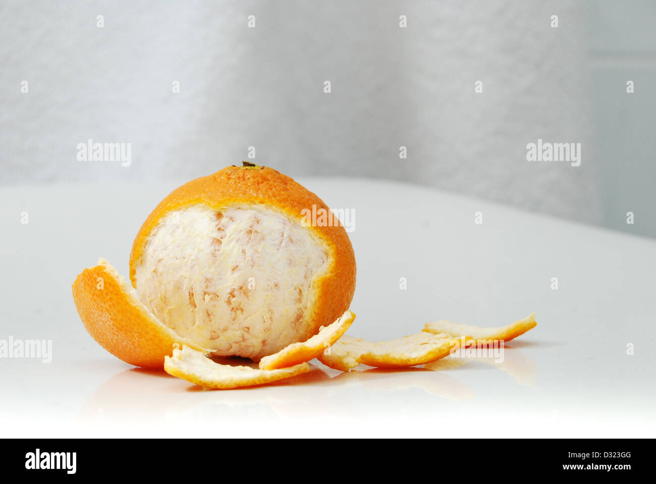 A partially peeled orange satsuma on a white background exposing some of the fruit flesh inside, surrounded by peel Stock Photo