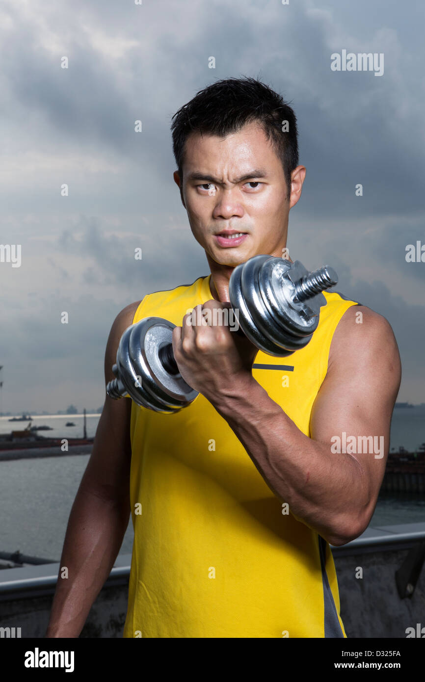 Athletic Young Chinese man exercising with dumbbells. Muscular Asian man exercising with weight training equipment. Stock Photo