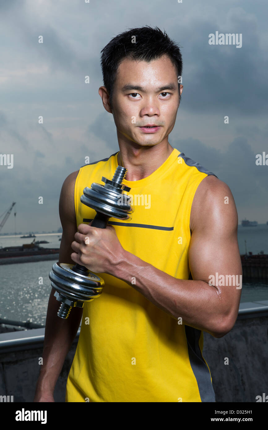 Athletic Young Chinese man exercising outdoors with dumbbells. Muscular
