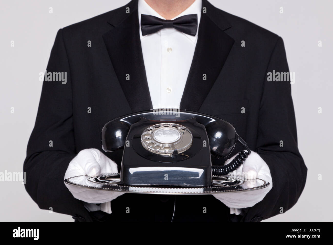 Butler holding a silver tray with an old retro black telephone on it. Stock Photo