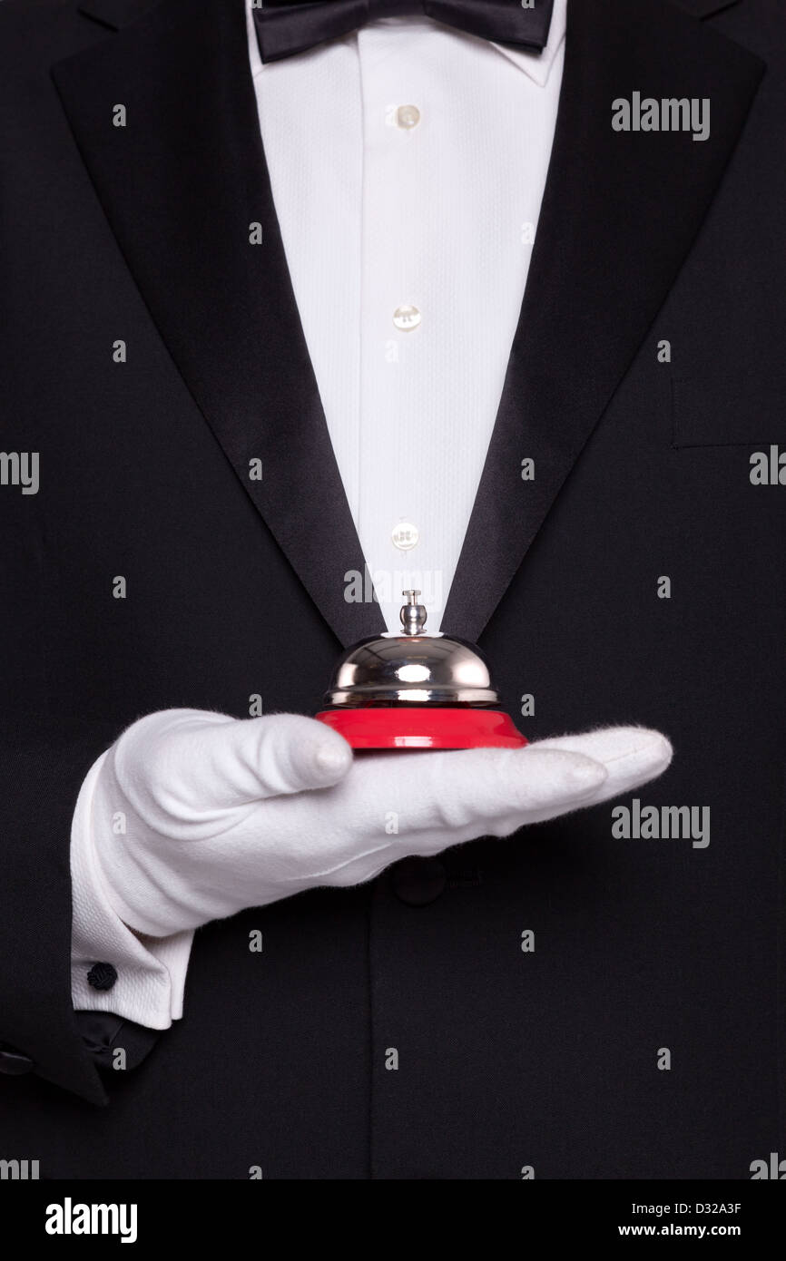 Waiter in black tie and white gloves holding a service bell. Stock Photo