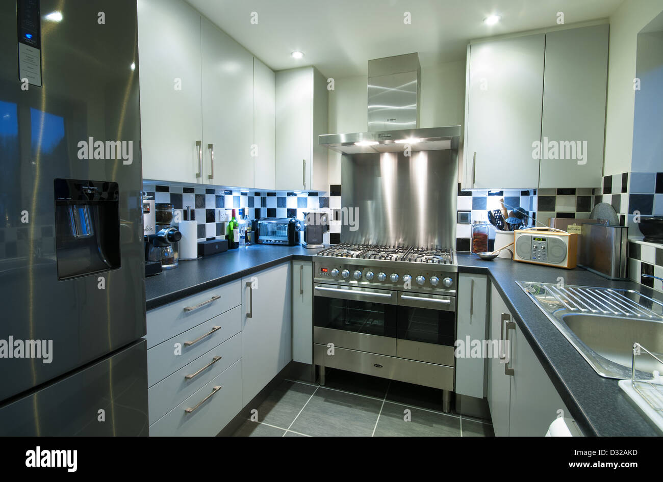A small, modern domestic kitchen with a fridge-freezer, range cooker and lots of storage space. UK, 2013. Stock Photo