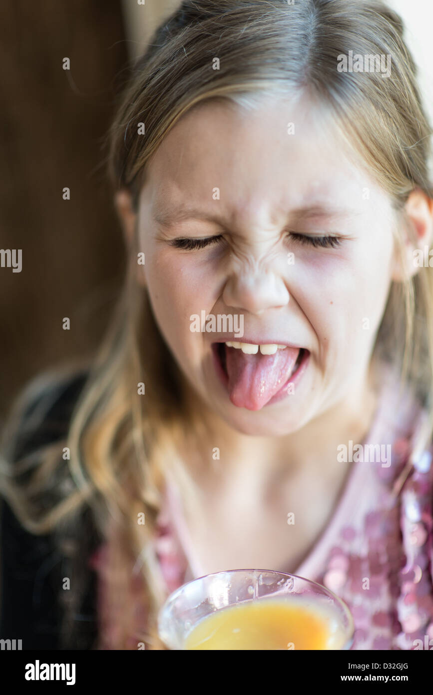 Young Girl with long hair pulling a funny face drinking sour orange juice Stock Photo