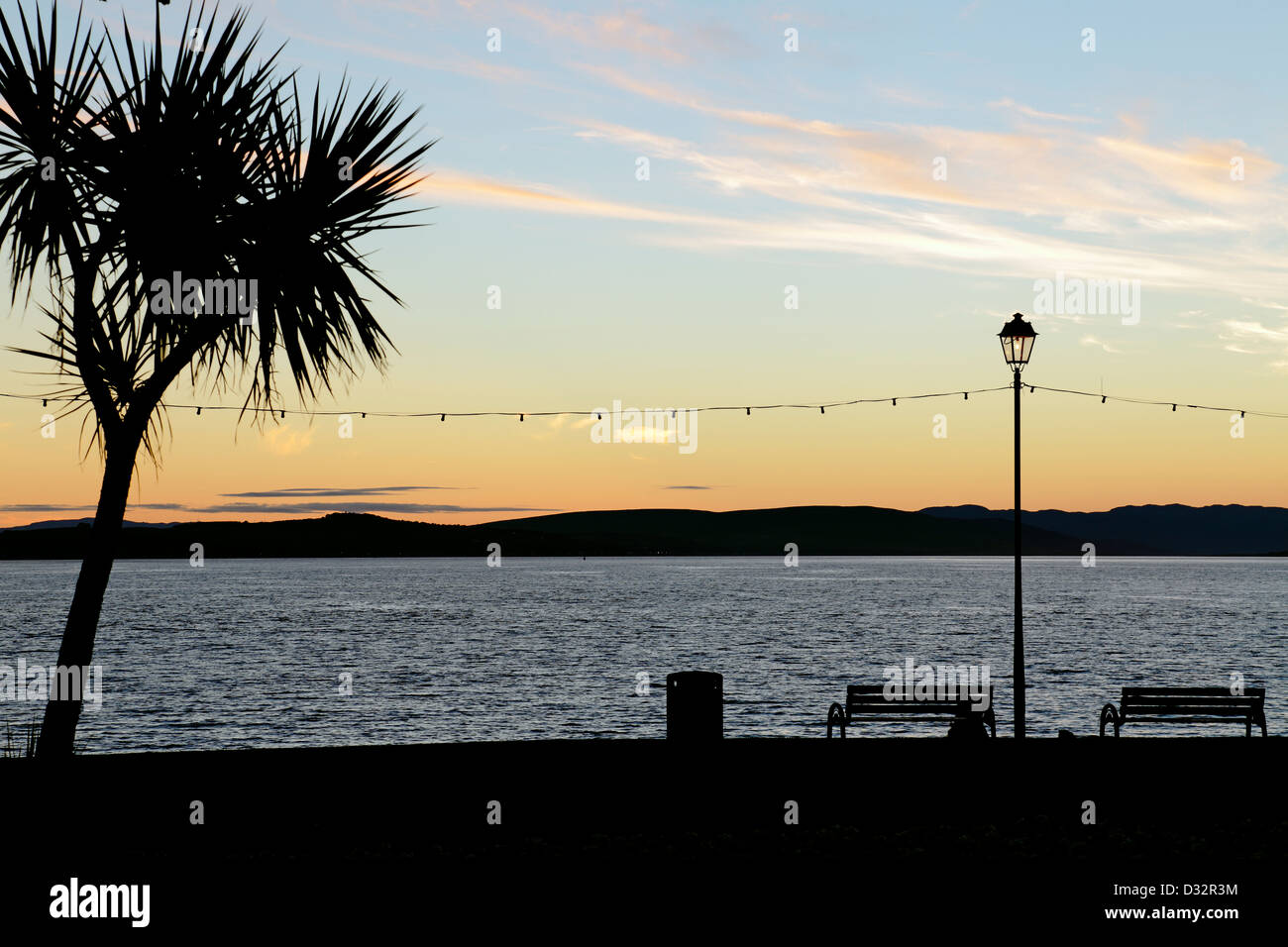 Palm tree, bench and lamp post at sunset beside the Firth of Clyde on ...