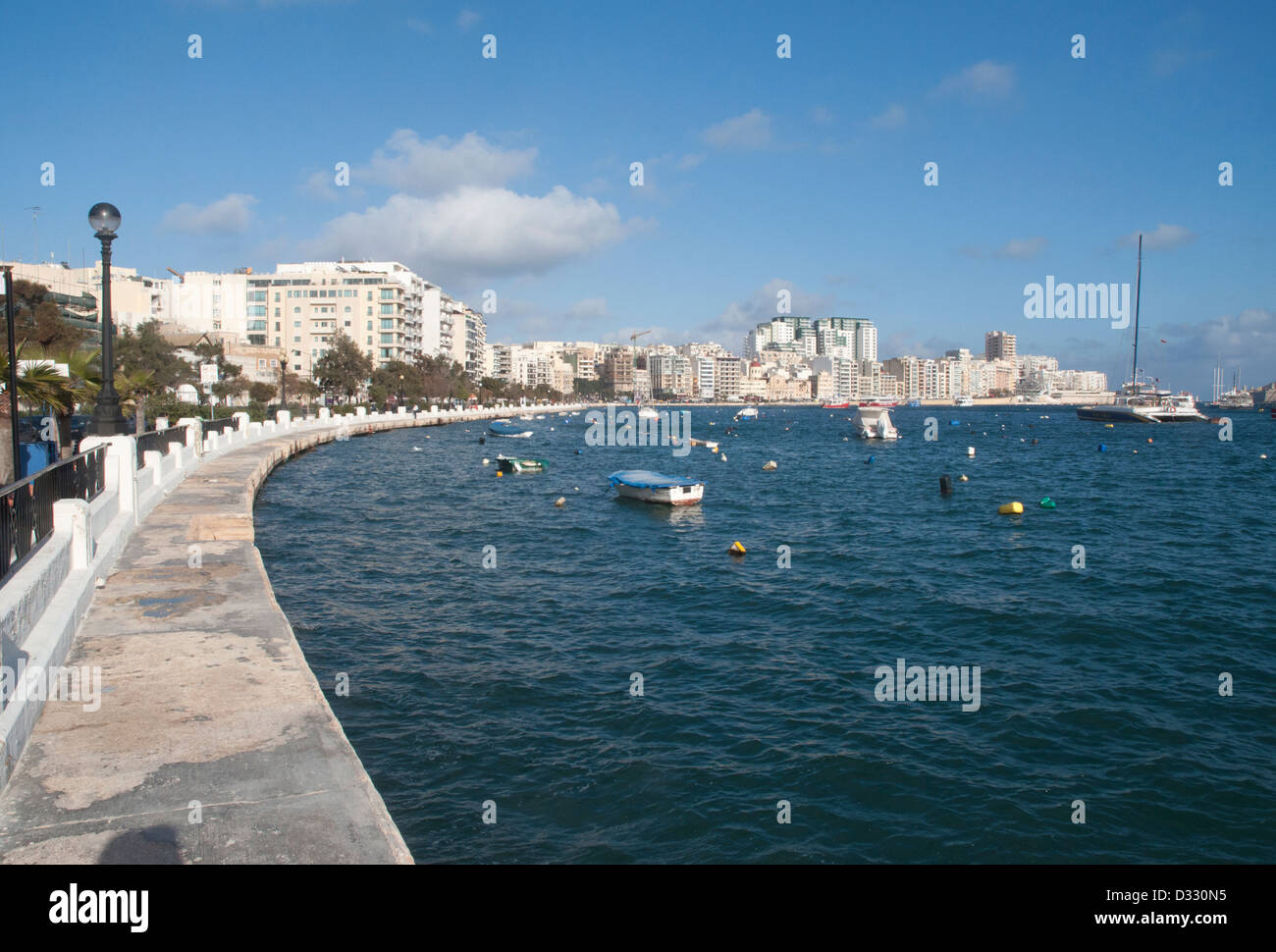 Sliema, Malta, promenade, treelined, street lamps, boats, water, harbour, tower blocks, blue sky, sunny Stock Photo