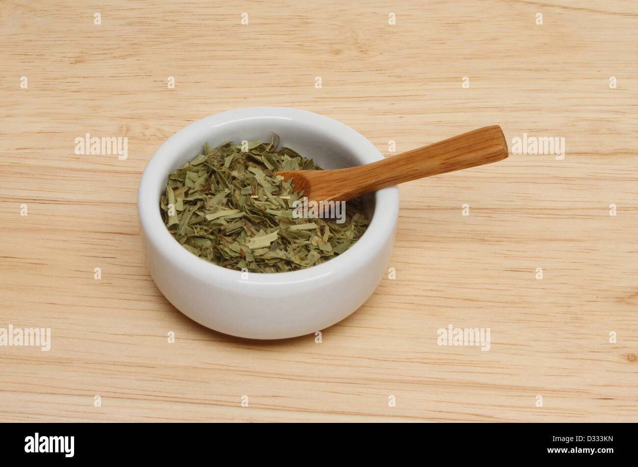 Dried tarragon herb leaves in a ramekin with a wood spoon on a wooden board Stock Photo