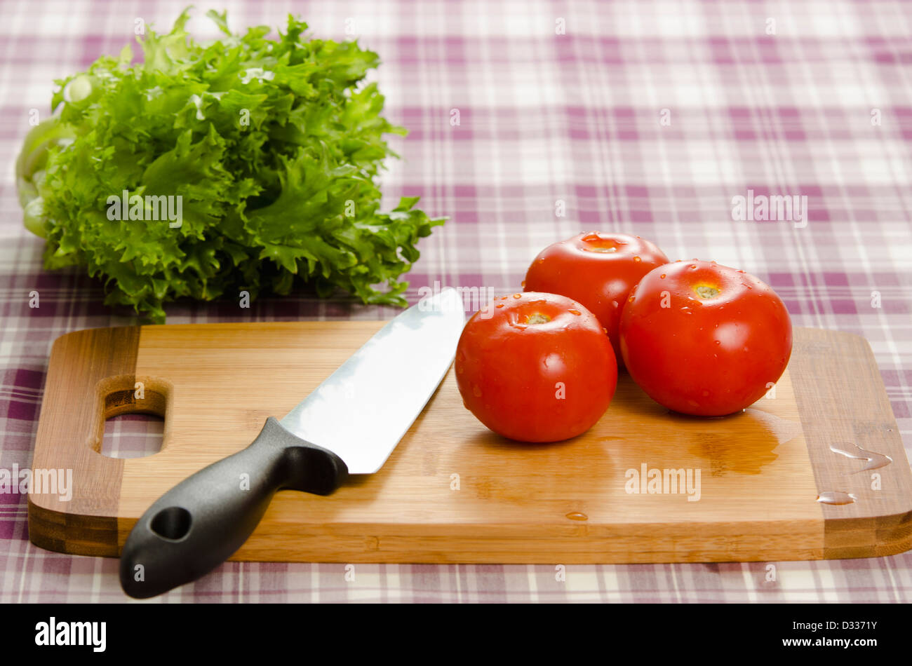 Tomatoes and lettuce on table with chopping board and knife. Healthy and fresh ingredients ready to be processed to food. Stock Photo