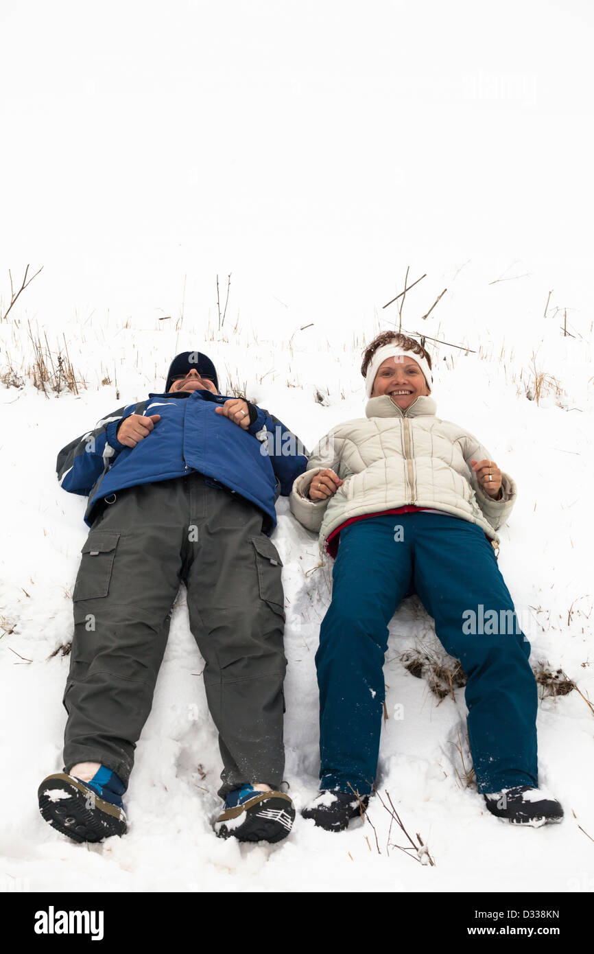 Happy middle aged couple relaxing on snow during winter vacation. Stock Photo