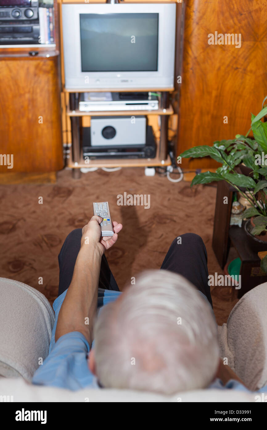 Senior man watching TV at home. Focus on remote control. Stock Photo
