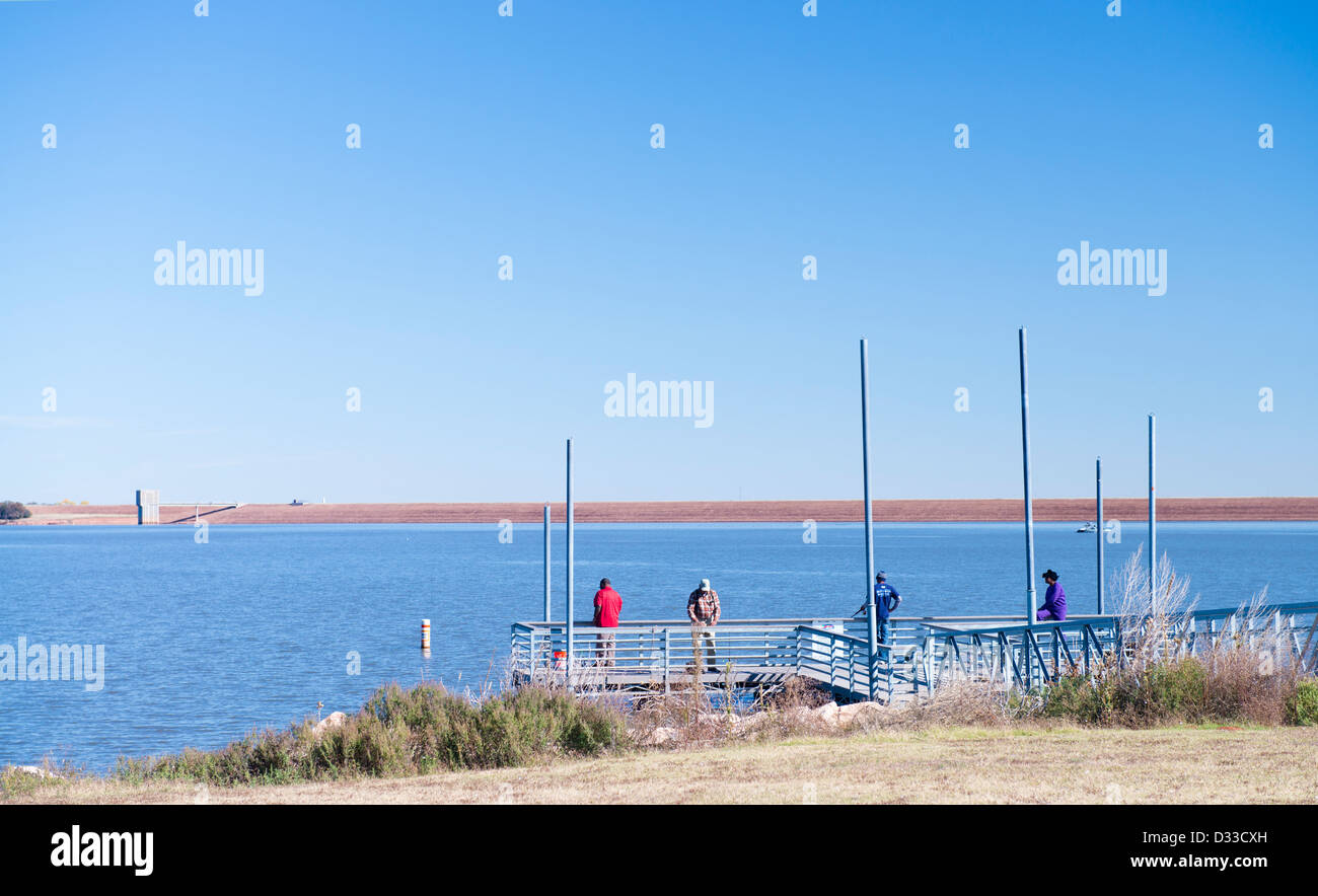Four people fish off the dock at Arcadia Lake in Oklahoma, USA.  In the background is the dam. Autumn. Stock Photo