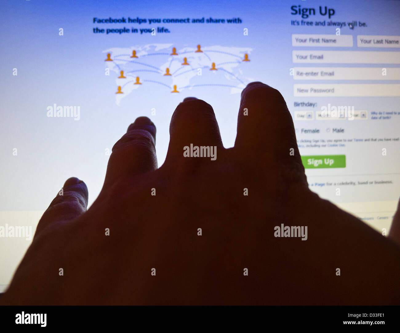 A hand reaching out towards the login page of Facebook on a computer screen. Stock Photo