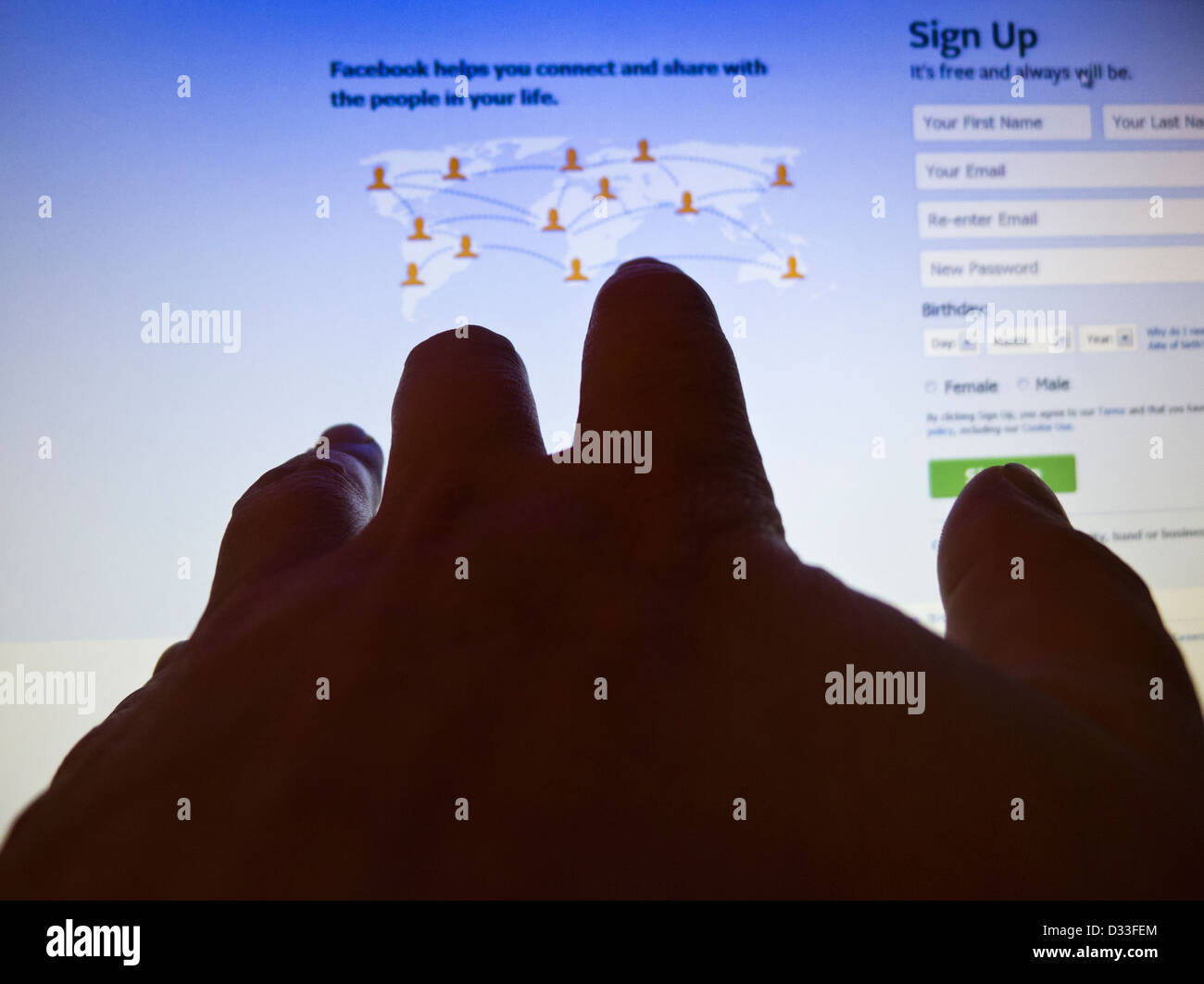 A hand reaching out towards the login page of Facebook on a computer screen. Stock Photo
