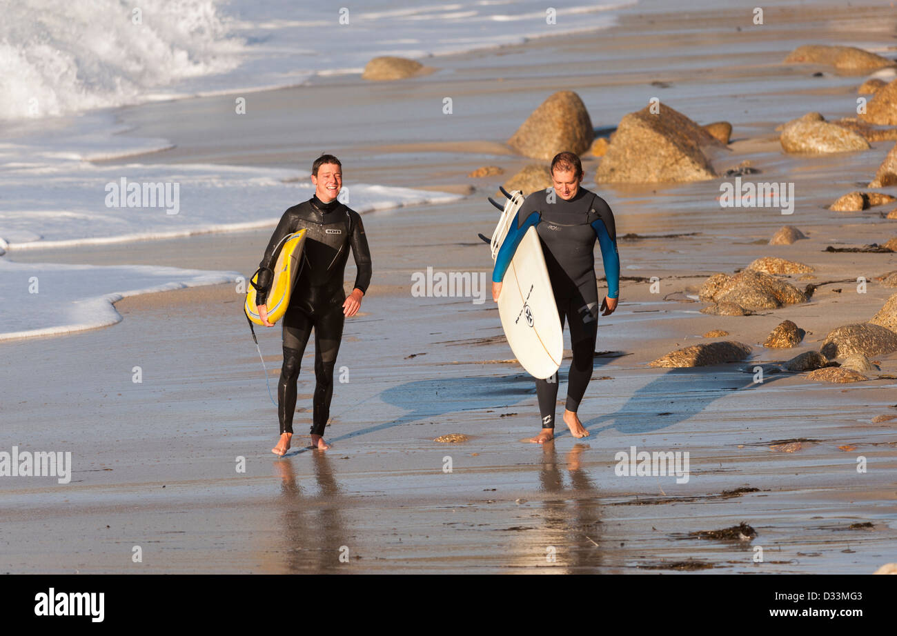 Two surfers walking along the beach at Sennen in Cornwall, England, UK Stock Photo