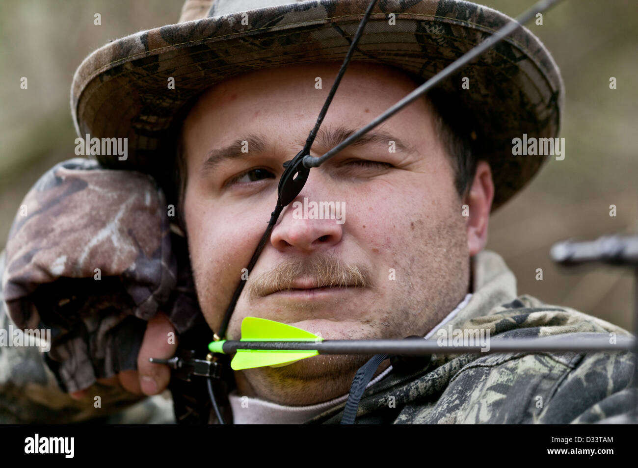 Man dressed in camouflage aiming bow and arrow while hunting for deer