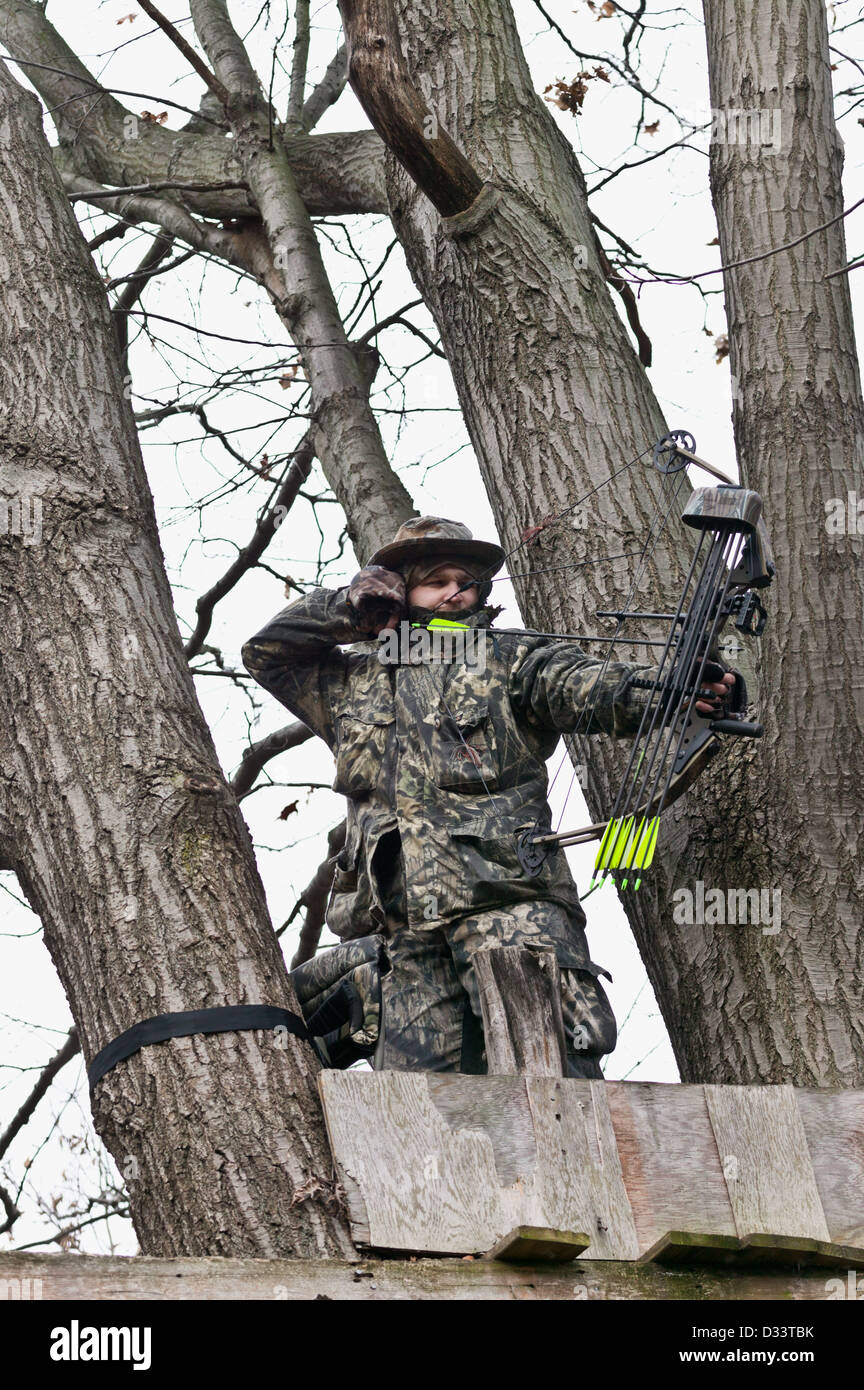 Man dressed in camouflage aiming bow and arrow while hunting for deer in the November woods, New