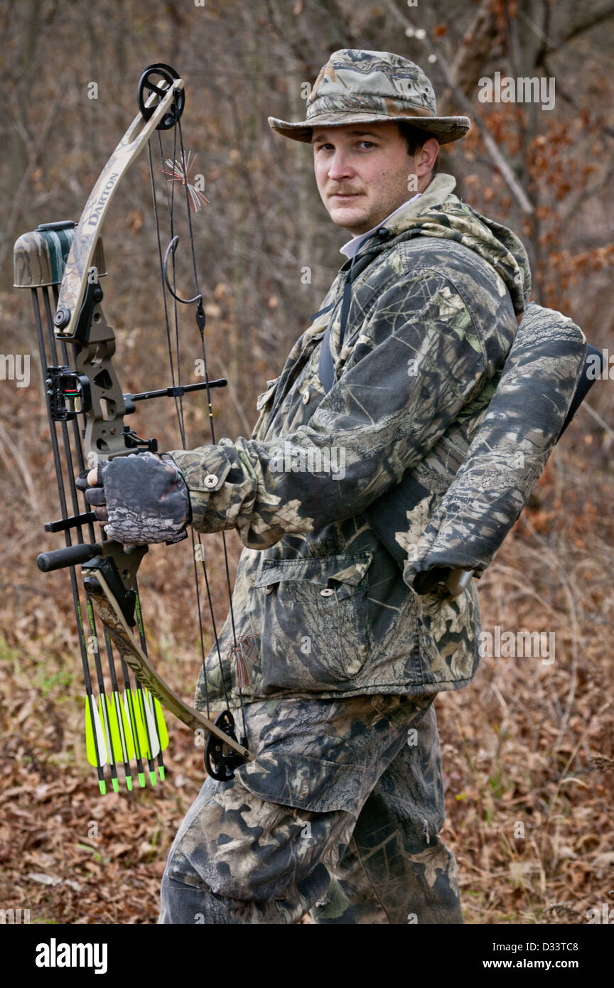 Man dressed in camouflage aiming bow and arrow while hunting for deer in the November woods, New