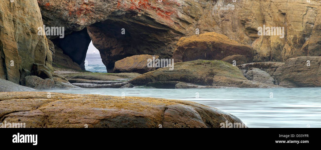 Beach with arch and light of boat in arch at Devil's Punchbowl State Natural Area. Oregon Stock Photo