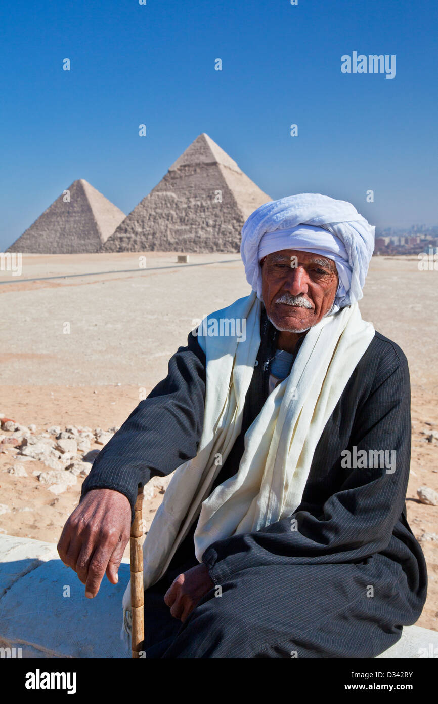 An elderly Arab on the Giza plateau, Egypt, with the Great Pyramids of Khufu or Cheops, and Khafre,or Chefren, in the background Stock Photo