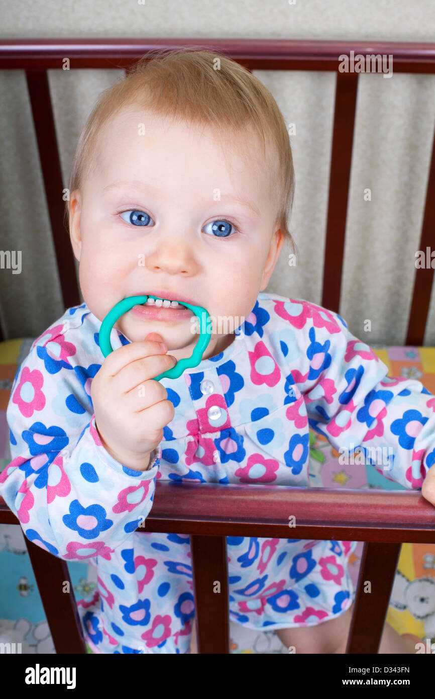 Little baby girl with blue eyes in a crib and keeps teeth teether Stock