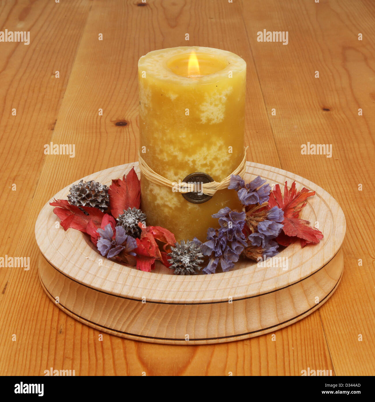 Burning yellow Feng Shui candle with potpourri in a wooden dish on a