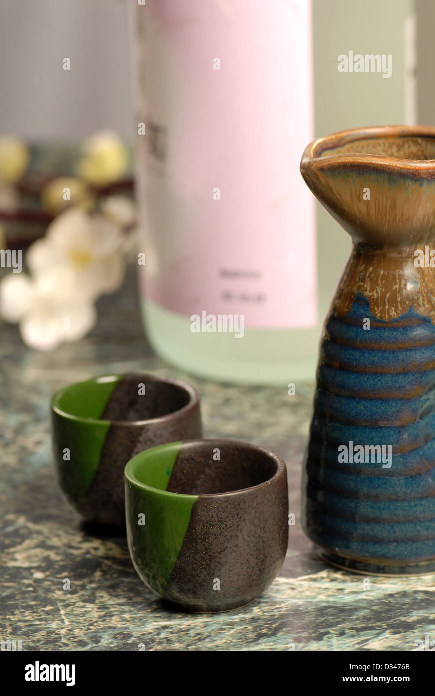 Japanese sake cups with bottle and flowers in background Stock Photo