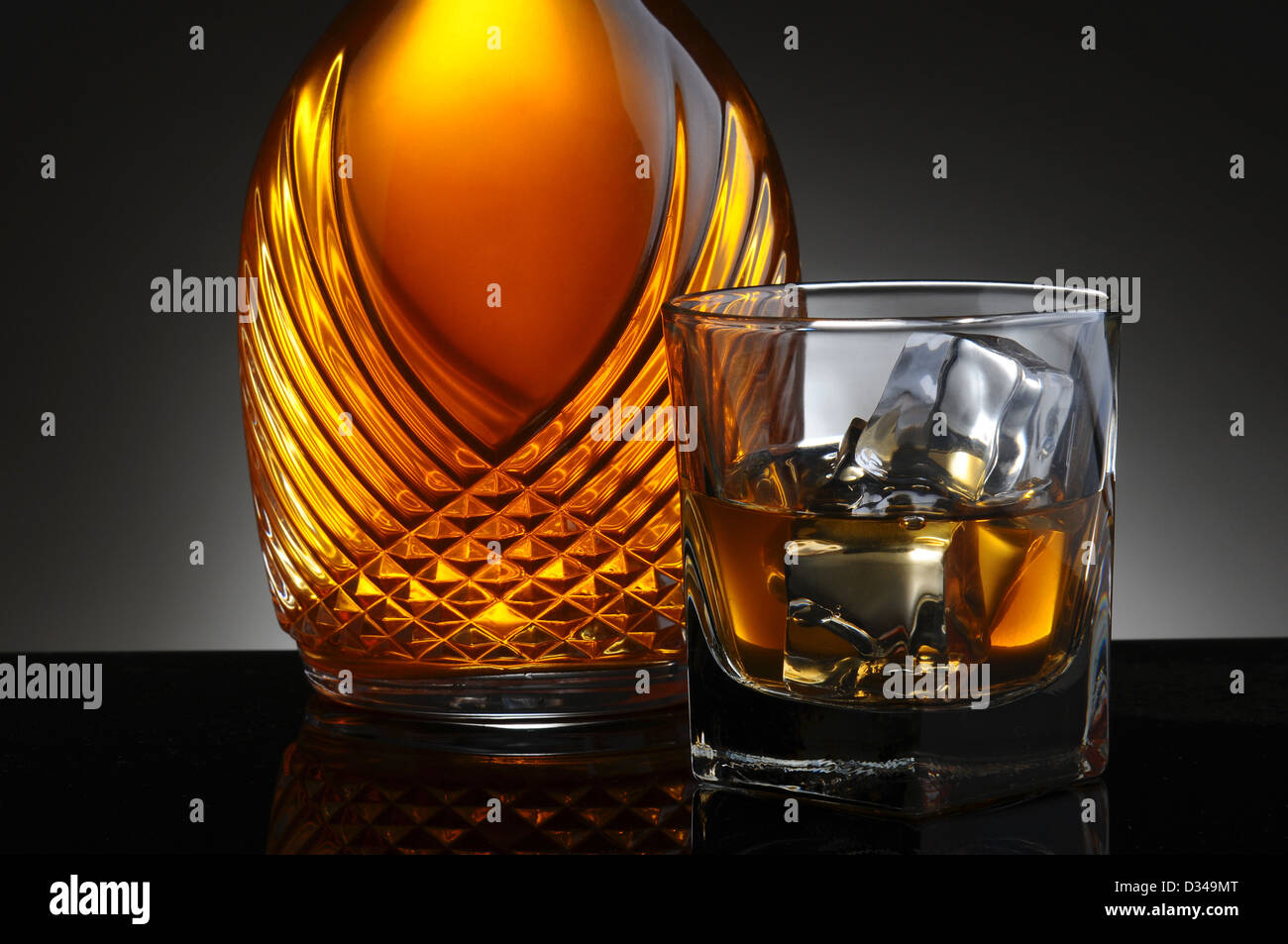 Closeup of an elegant decanter and a glass of scotch on the rocks. Horizontal format on a light to dark gray background. Stock Photo