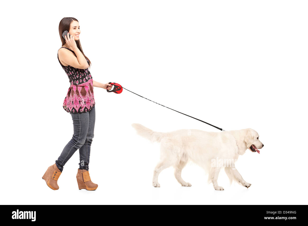 Full length portrait of a young female walking her dog and talking on a mobile phone isolated on white background Stock Photo