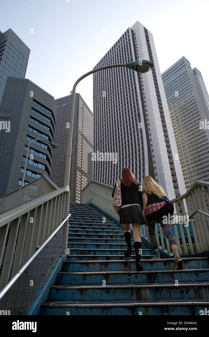 Girls ascending a pedestrian overpass with corporate skyscrapers looming overhead in Tokyo's West Shinjuku business district. Stock Photo