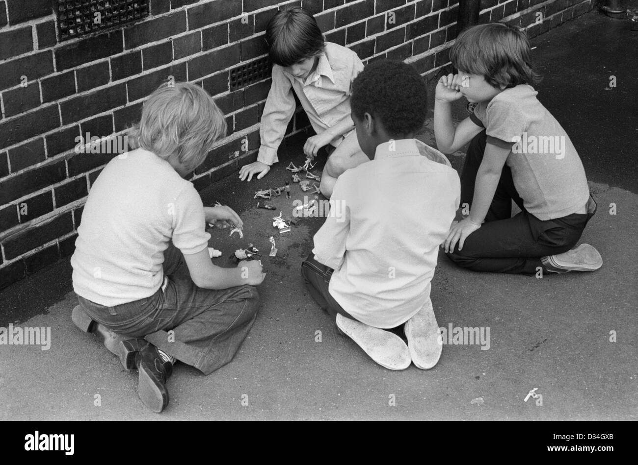 Playground games. South London junior school 1970s England. Multi ethnic group boys playing with toy soldiers.1975 UK HOMER SYKES Stock Photo