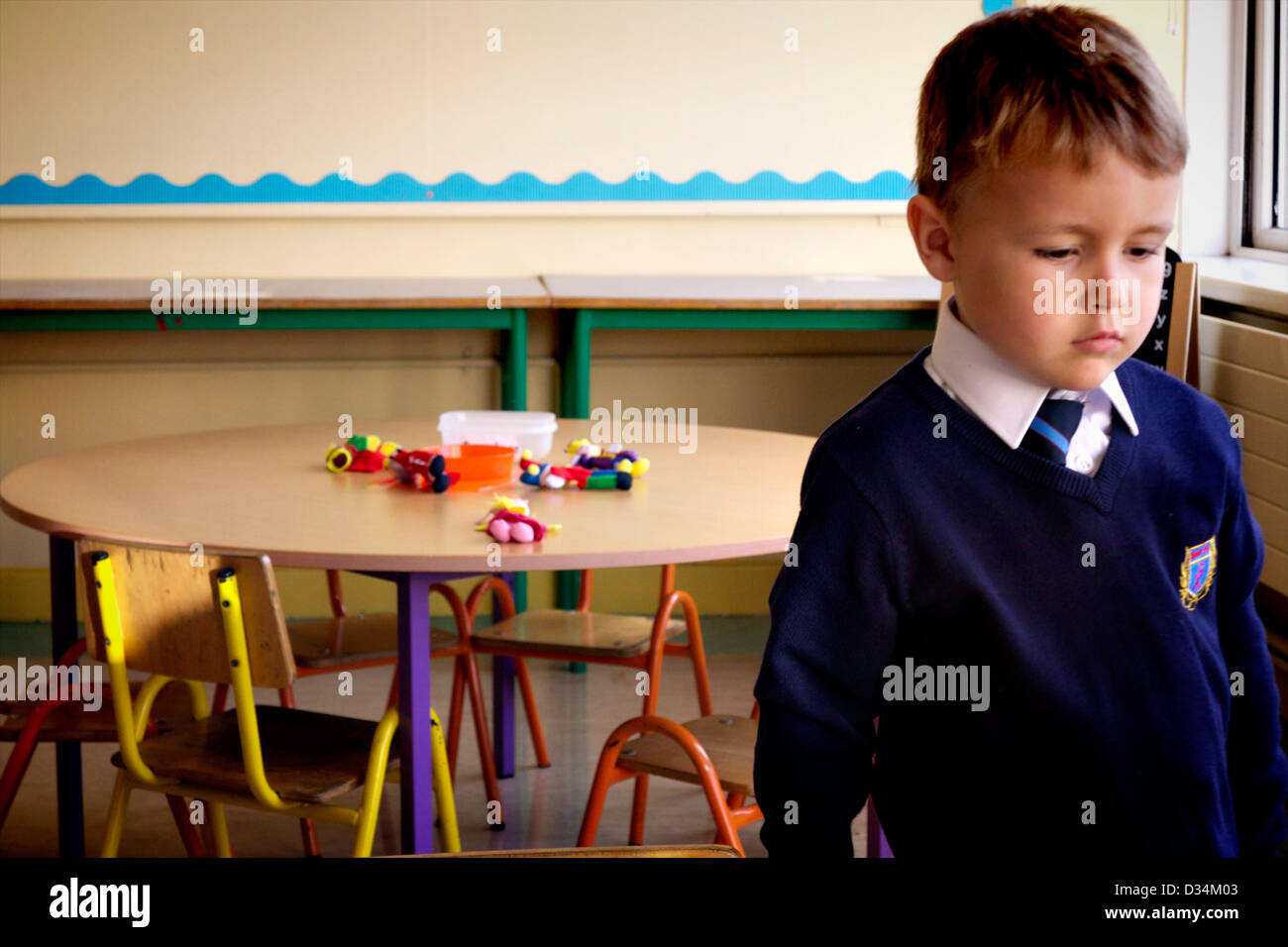 Small boy on his first day in school, alone in the classroom with group table and toys on it. Stock Photo