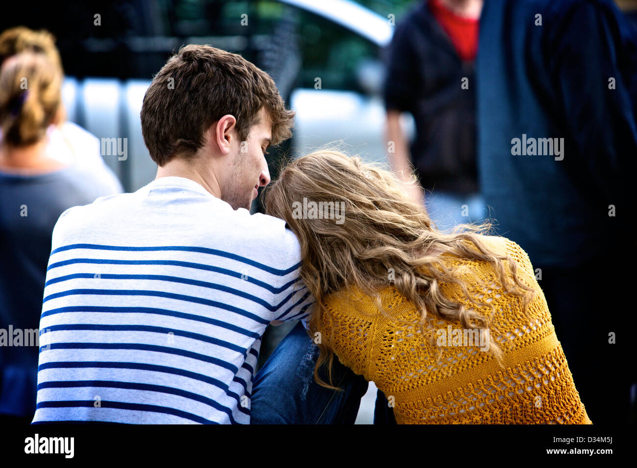 A young couple, a blonde girl and boy show affection whilst sitting. Stock Photo