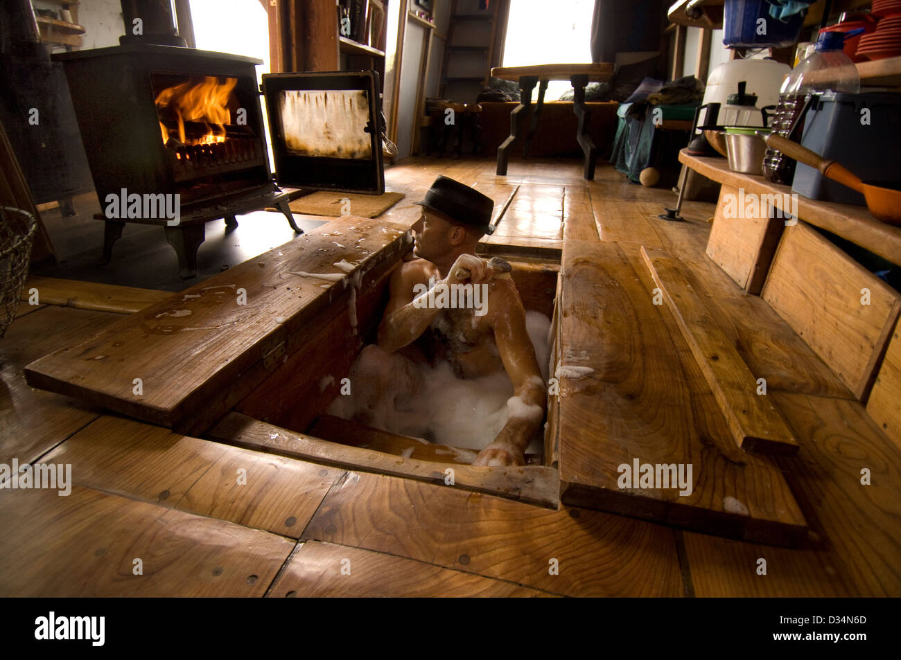 Man in a hat in the underfloor bath of his hand-made caravan home. Stock Photo