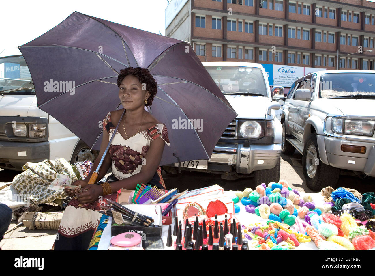 A street vendor in Lusaka City Market sitting under an umbrella selling cosmetic products. Stock Photo
