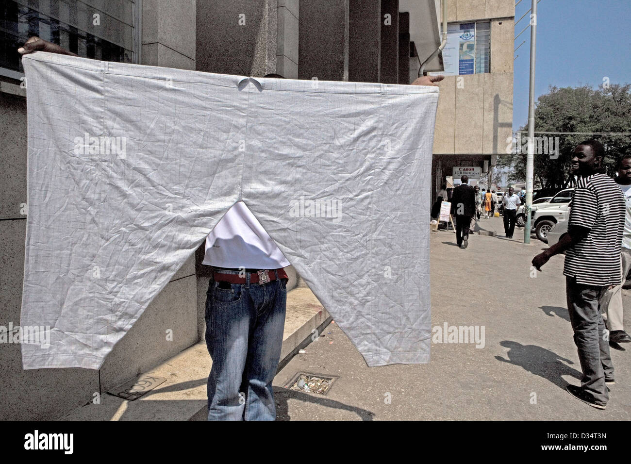 A street vendor in the capital of Zambia, Lusaka holding up a pair of large oversized pants he is hoping to sell. Stock Photo