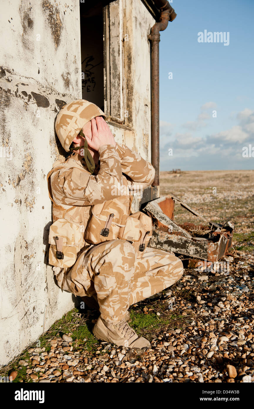 Soldier resting against the wall of a bombed out building, with his hands covering his face. Stock Photo
