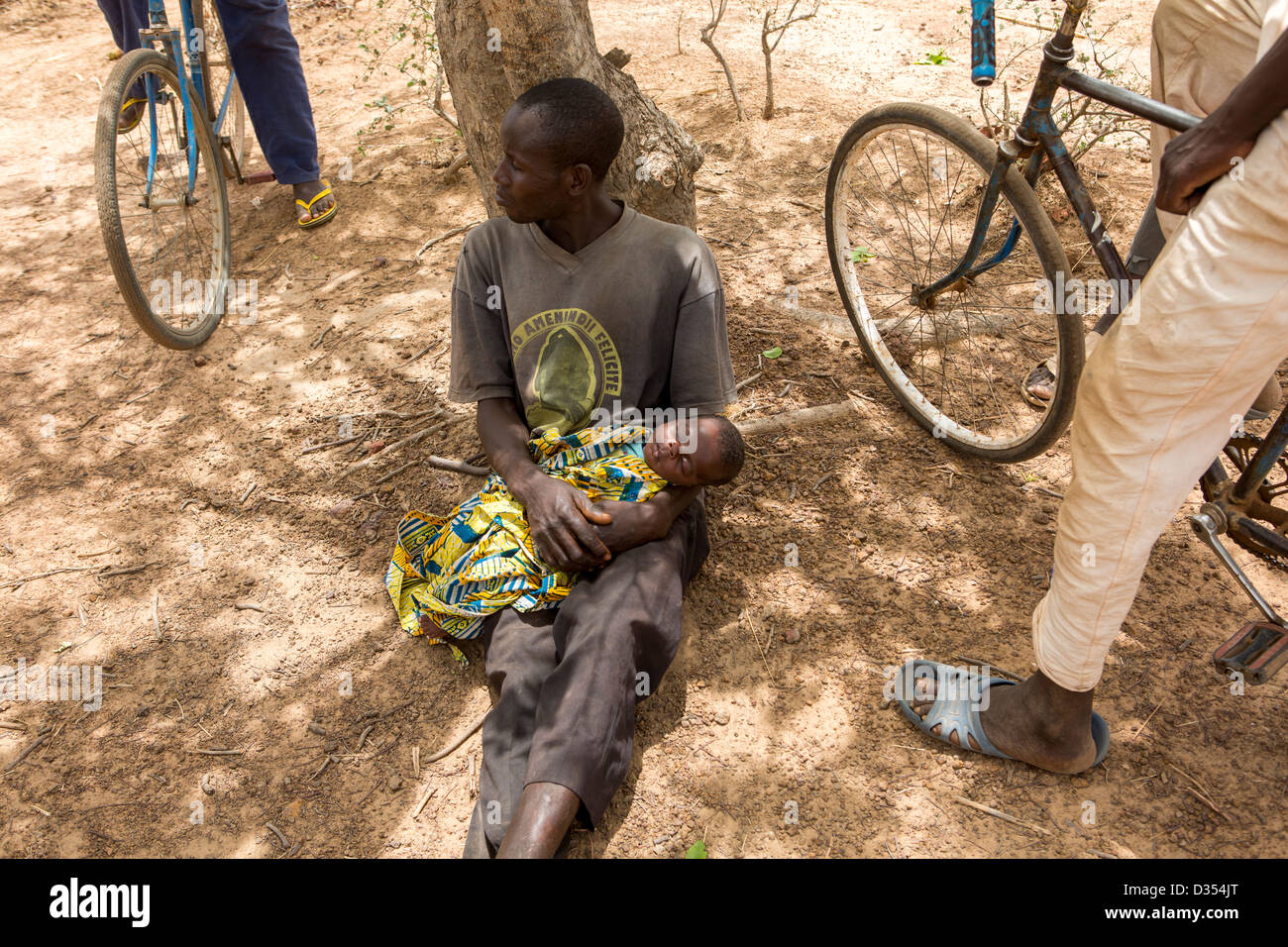 Yako, Burkina Faso, May 2012: A father looks after his daughter while his wife picks wild fruit nearby. Stock Photo