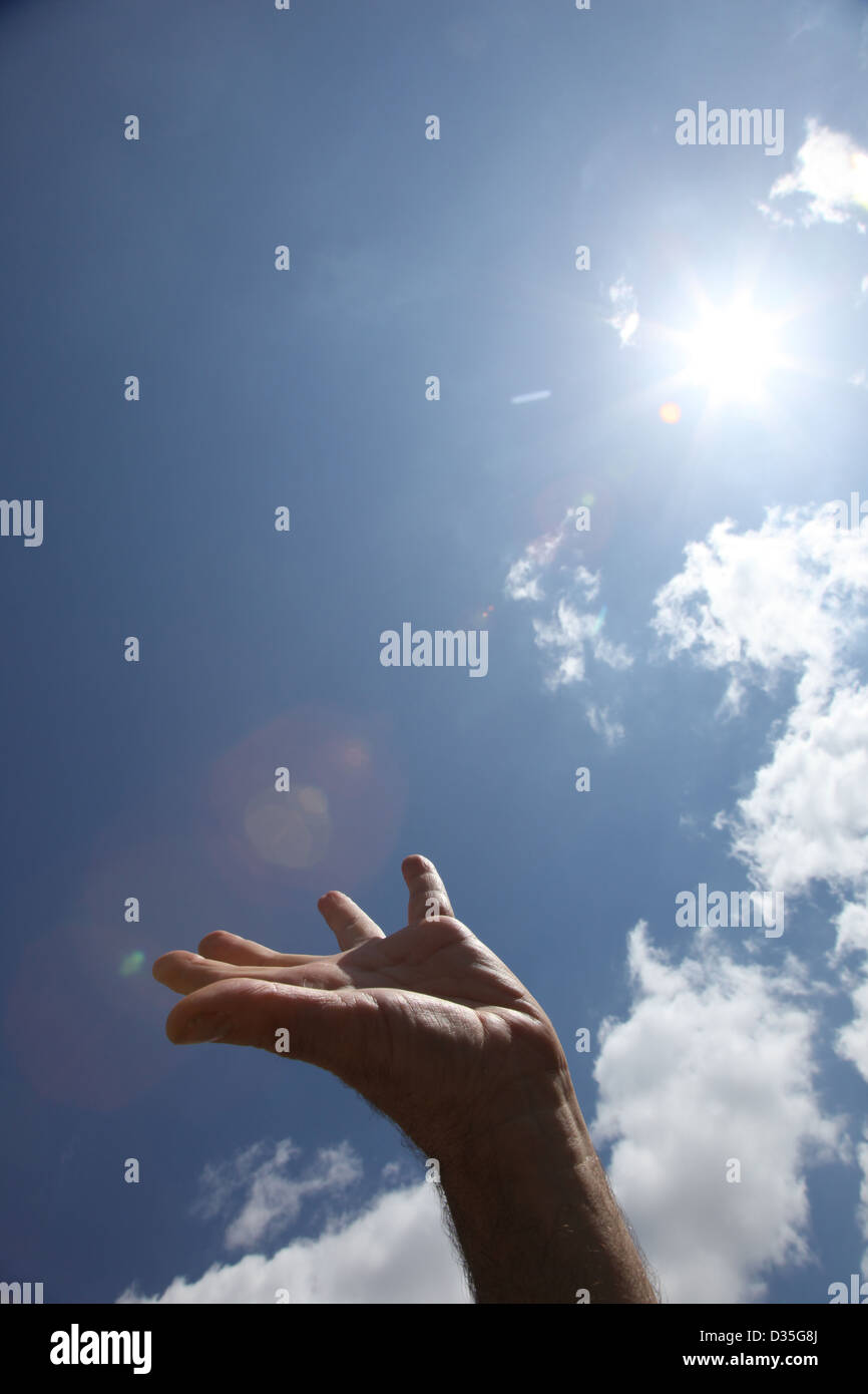 A male hand reaches up to the sun burning bright in the sky, palm facing upwards. Stock Photo