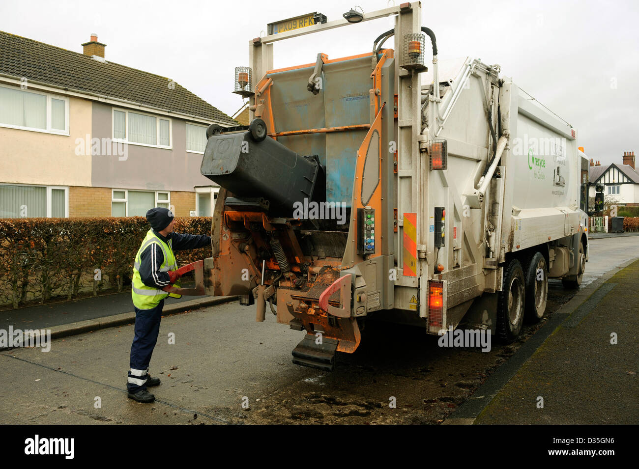 Refuse collection. A bin man empties wheelie bins of rubbish, garbage, trash into a waste