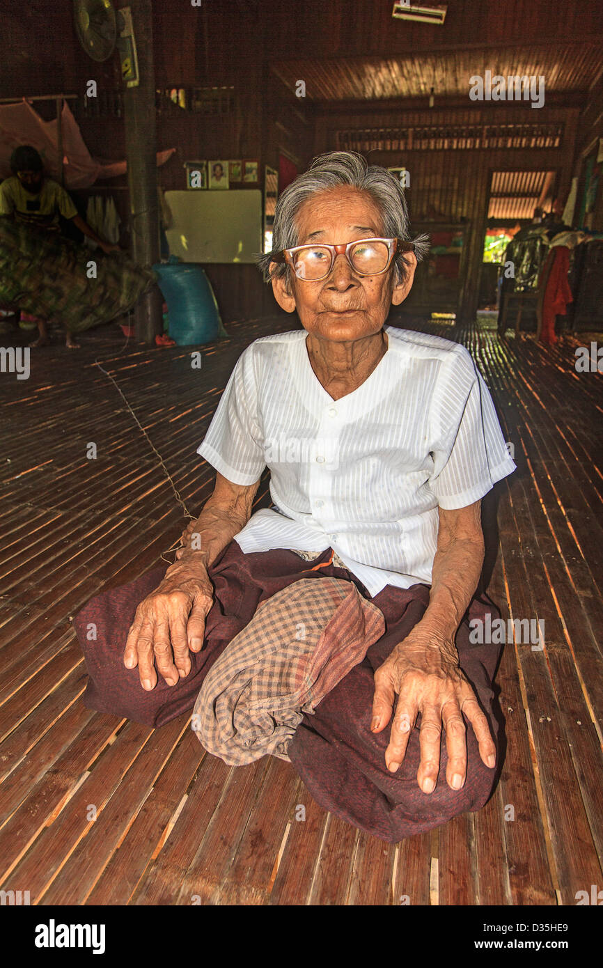 Eldery woman sits on mahogany wood slat floor of her house on Koh Trong