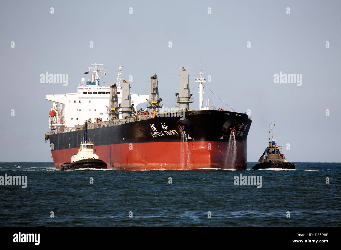 Bulk carrier ship escorted by two tugboats into Newcastle Australia to load coal from the Hunter Valley coal fields Stock Photo