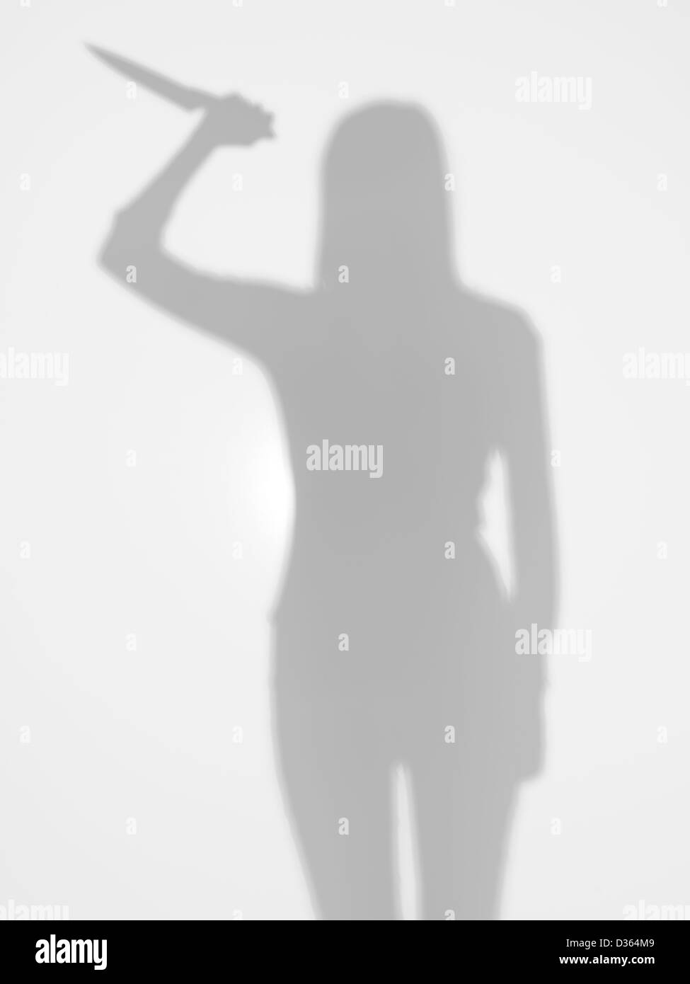 female silhouette holding a knife in her hand with a gesture of attack, behind a diffuse surface  Stock Photo