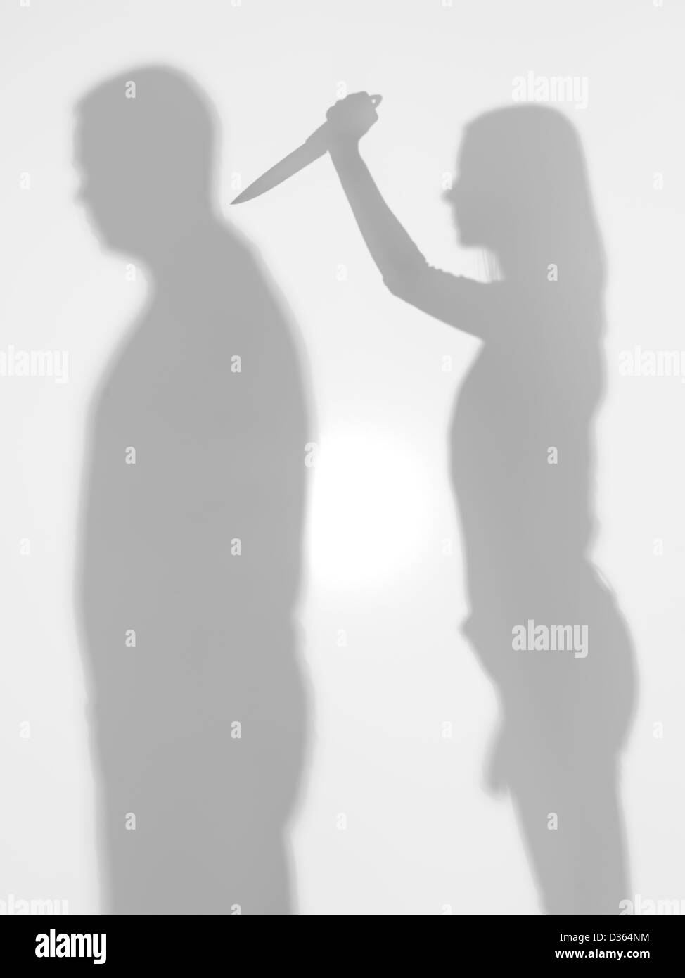 body silhouettes standing from profile, woman trying to stab a man with a kitchen knife, behind a diffuse surface Stock Photo